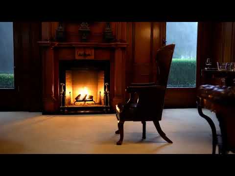 A room with a fireplace inside and rain falling outside through glass